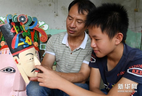 方文展在给儿子方庭源（右）讲述毛南族傩面的雕刻技巧