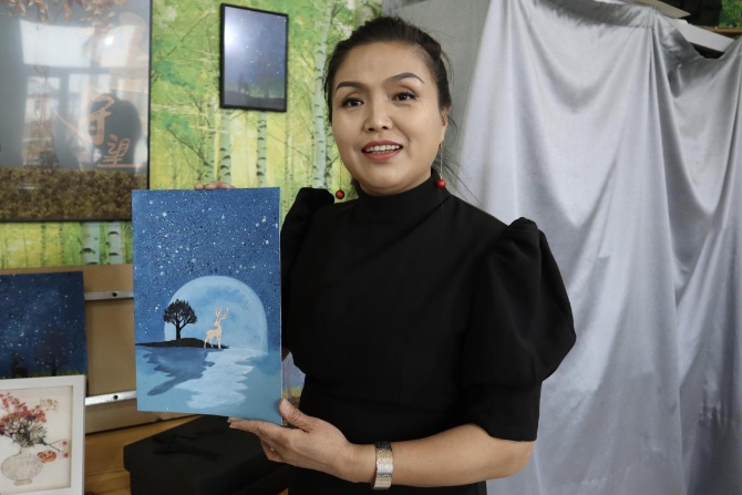 (李艳红和《星空鹿》树皮画 央视网记者 王静远 摄)