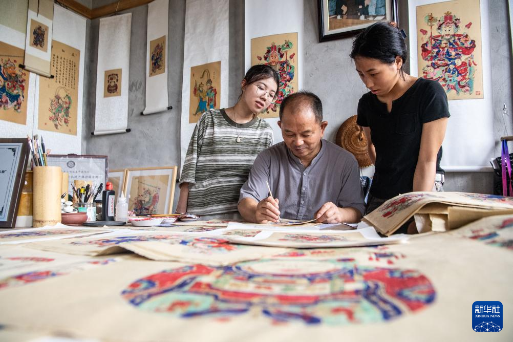 8月10日，梁平木版年画代表性传承人徐家辉（中）在演示年画上色。